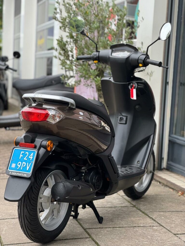 Bruine scooter vanaf achterzijde op standaard, geparkeerd voor een winkel.