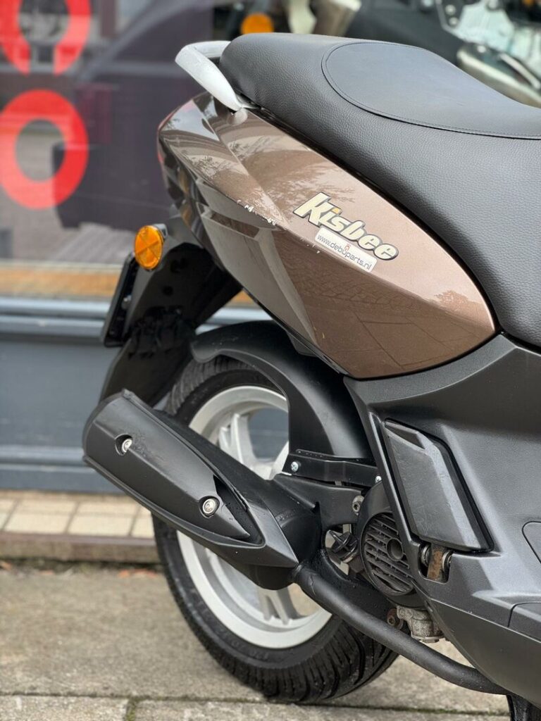 Close-up van de achterzijde van een bruine Peugeot Kisbee scooter met uitlaat, wiel en zadel.