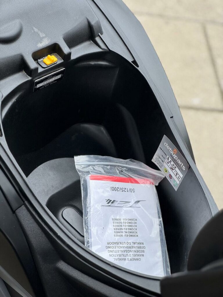 Opbergruimte onder het zadel van een scooter met handleiding in plastic zak