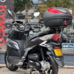 Zwarte scooter met topkoffer en geel kenteken, op de standaard bij showroom.