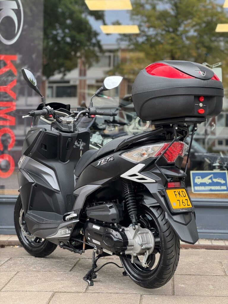 Zwarte scooter met topkoffer en geel kenteken, op de standaard bij showroom.