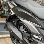 Close-up van de achterzijde van een zwarte scooter met zadel, uitlaat en achterwiel.