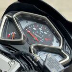 Close-up van het dashboard van een SYM-motor, met analoge snelheidsmeter en brandstofmeter.