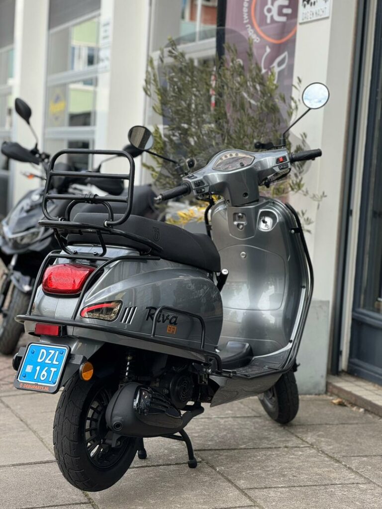 Grijze Riva-scooter met blauw Nederlands kenteken, geparkeerd voor een winkelpui.