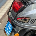 Achterkant van een grijze scooter met bagagerek, achterlicht en blauwe kentekenplaat.