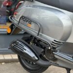Close-up van de achterzijde van een grijze Riva EFI scooter met uitlaat, wiel en bagagedrager.