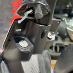 Close-up van het stuur, dashboard, remhendel en voetplaat van een zwarte scooter in zonlicht.