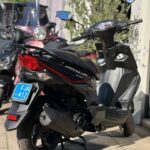 Zwarte scooter met rode accenten op de middenbok, buiten voor een winkel.