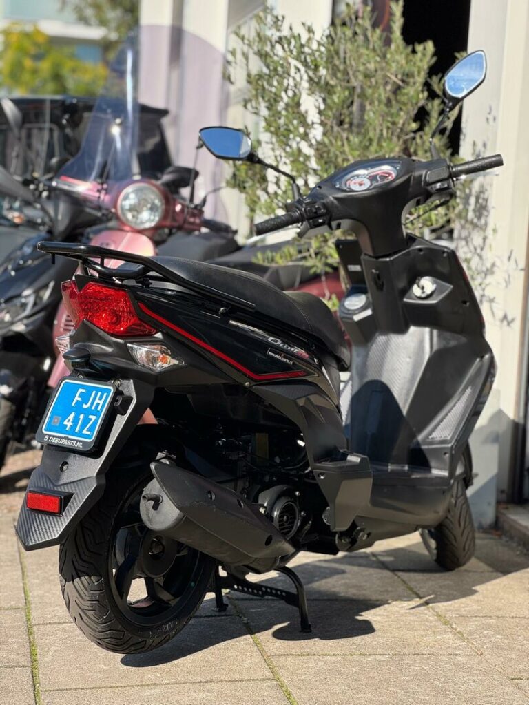 Zwarte scooter met rode accenten op de middenbok, buiten voor een winkel.