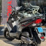 Moderne grijze scooter op middenstandaard voor een motorzaak, gezien van achteren.