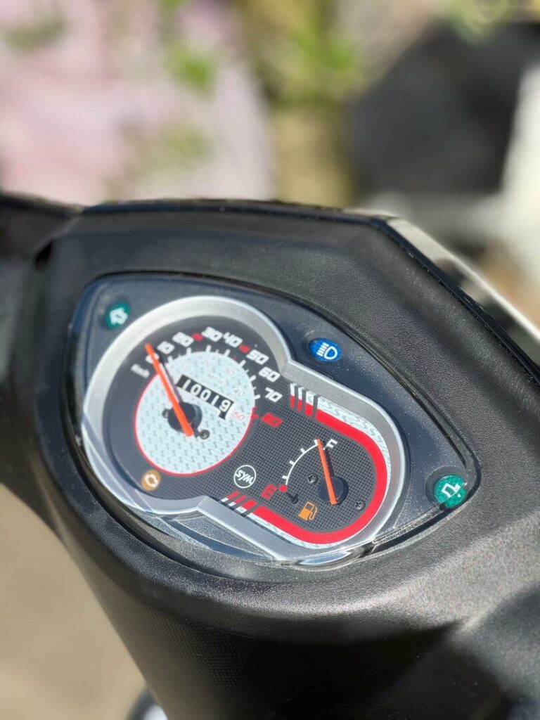 Close-up van het dashboard van een scooter met snelheidsmeter, brandstofmeter en kilometerteller op 10019 km.
