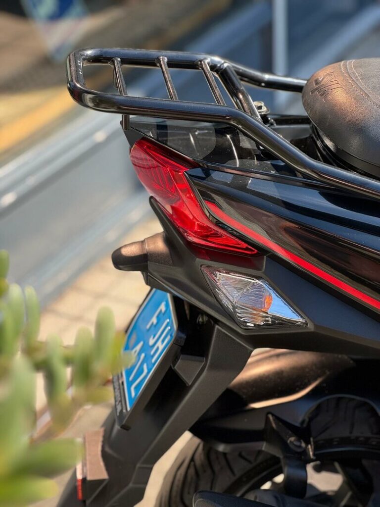 Close-up van de achterkant van een zwarte scooter met bagagerek, rode achterlamp en blauwe kentekenplaat.