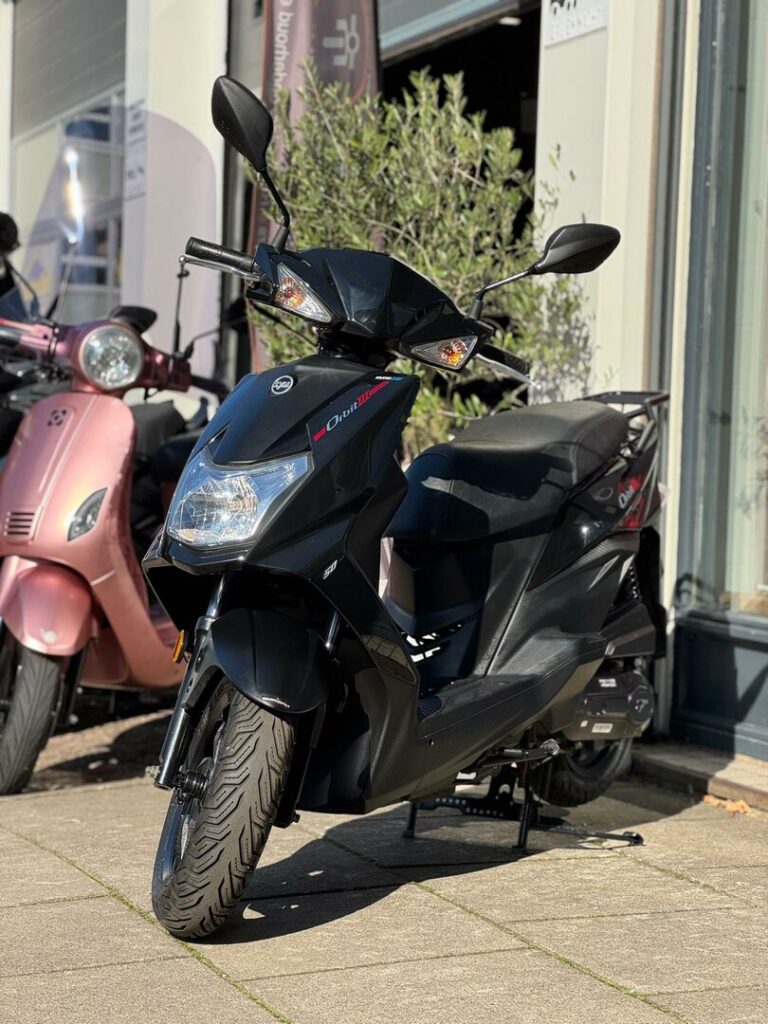 Zwarte scooter op standaard voor een winkel, met roze scooter op de achtergrond.