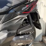 Close-up van de achterzijde van een zwarte scooter met zadel, vering en motorbehuizing.