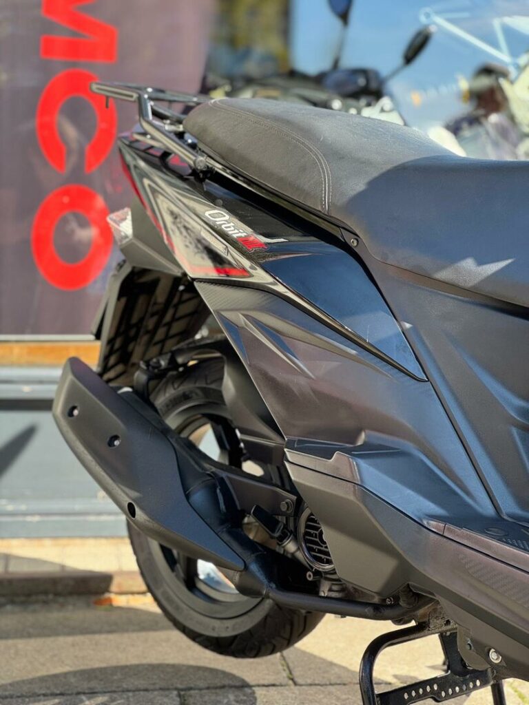 Close-up van de achterkant van een zwarte scooter met uitlaat, achterwiel en zadel.