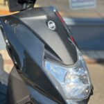 Close-up van de voorkant van een zwarte SYM-scooter met koplamp en logo.