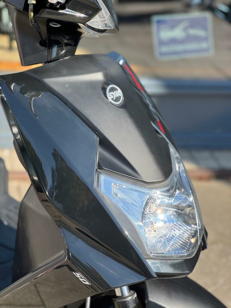 Close-up van de voorkant van een zwarte SYM-scooter met koplamp en logo.