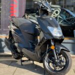 Zwarte motorscooter op zijn middenbok voor een showroom, close-up rechtsvoor.