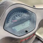 Close-up van het dashboard van een scooter met toerenteller en digitaal display, 0 km/u en 6379 km op de teller.