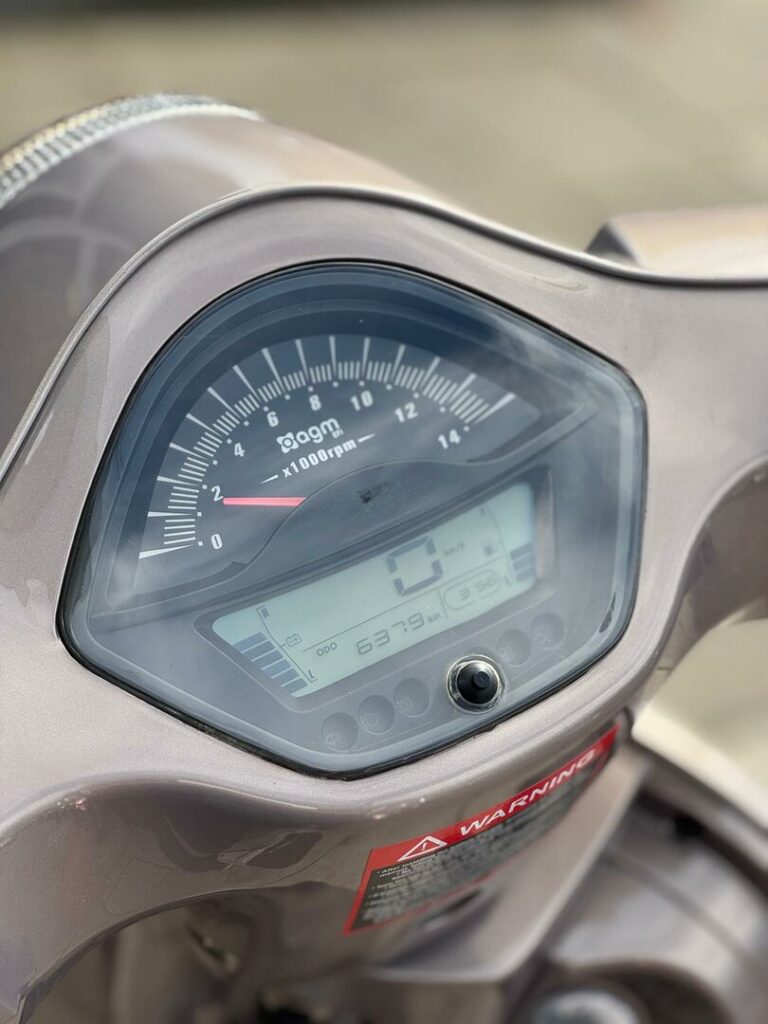 Close-up van het dashboard van een scooter met toerenteller en digitaal display, 0 km/u en 6379 km op de teller.