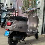 Lichtbruine AGM VX50 S scooter met achterdrager en spiegels, geparkeerd voor een showroom.