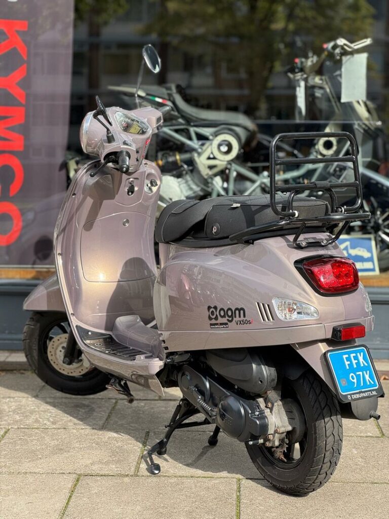 Zandkleurige AGM VX50s scooter op standaard, buiten voor een showroom.
