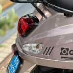 Close-up van de achterzijde van een scooter met rood achterlicht, knipperlicht en blauwe kentekenplaat.