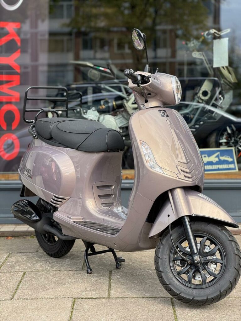Beige glanzende retro scooter met bagagedrager, geparkeerd voor een motorwinkel.