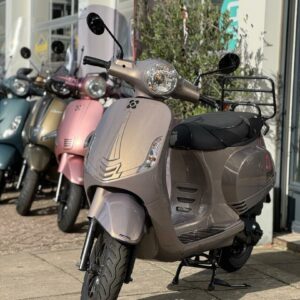 Beige metallic scooter met ronde koplamp op de standaard voor een showroom, met meerdere scooters op de achtergrond.