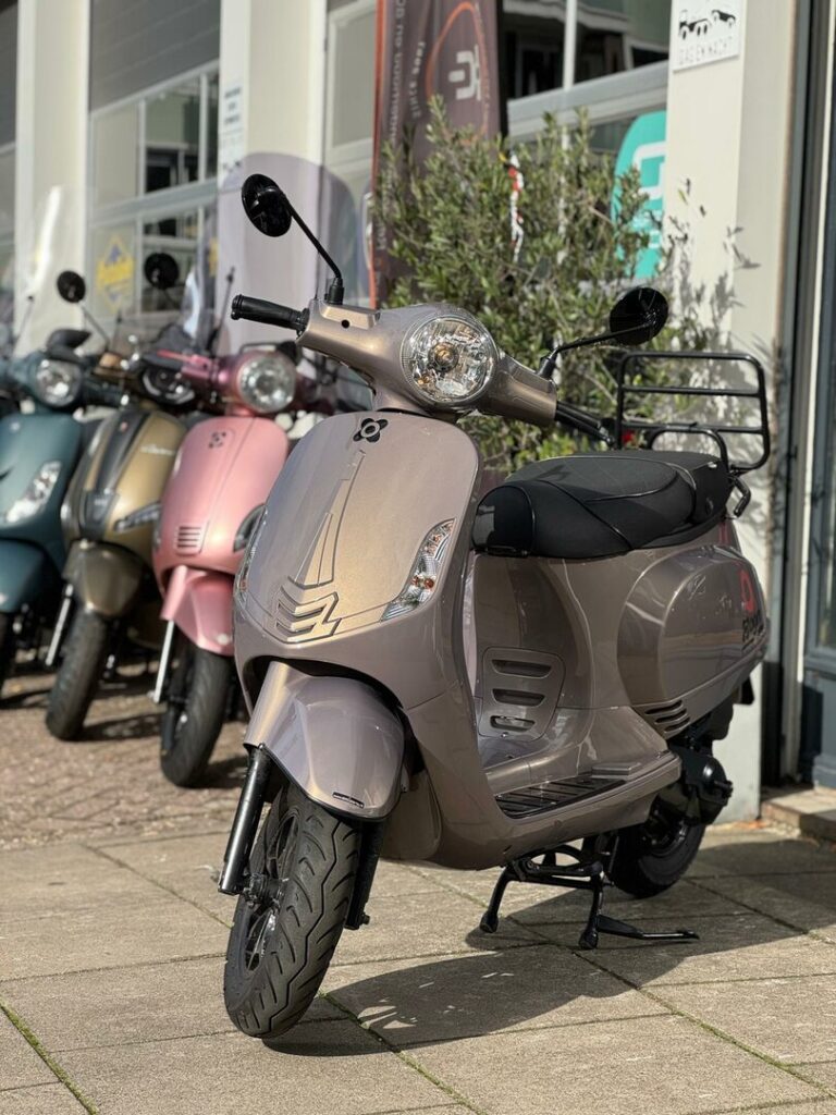 Beige metallic scooter met ronde koplamp op de standaard voor een showroom, met meerdere scooters op de achtergrond.