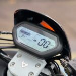 Close-up van digitaal motorinstrumentenpaneel met snelheid 0 km/u en batterij-indicator.