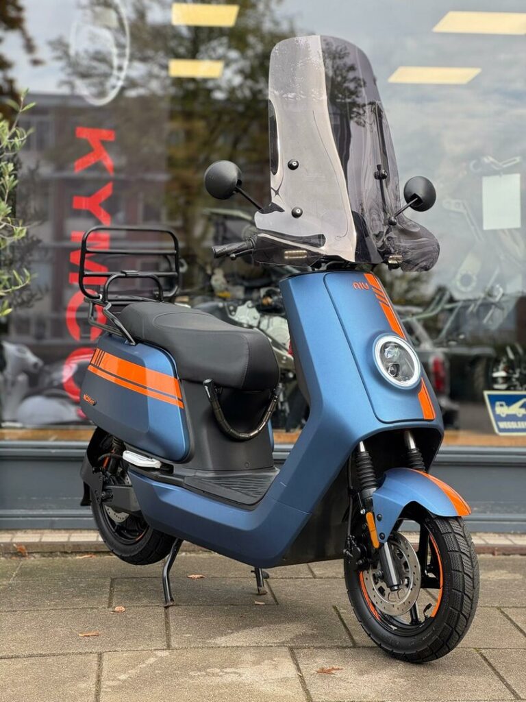 Blauw-oranje elektrische scooter met hoog windscherm, geparkeerd voor een winkel