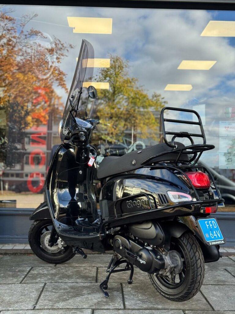 Zwarte scooter met windscherm en bagagedrager, geparkeerd voor een winkelpui.
