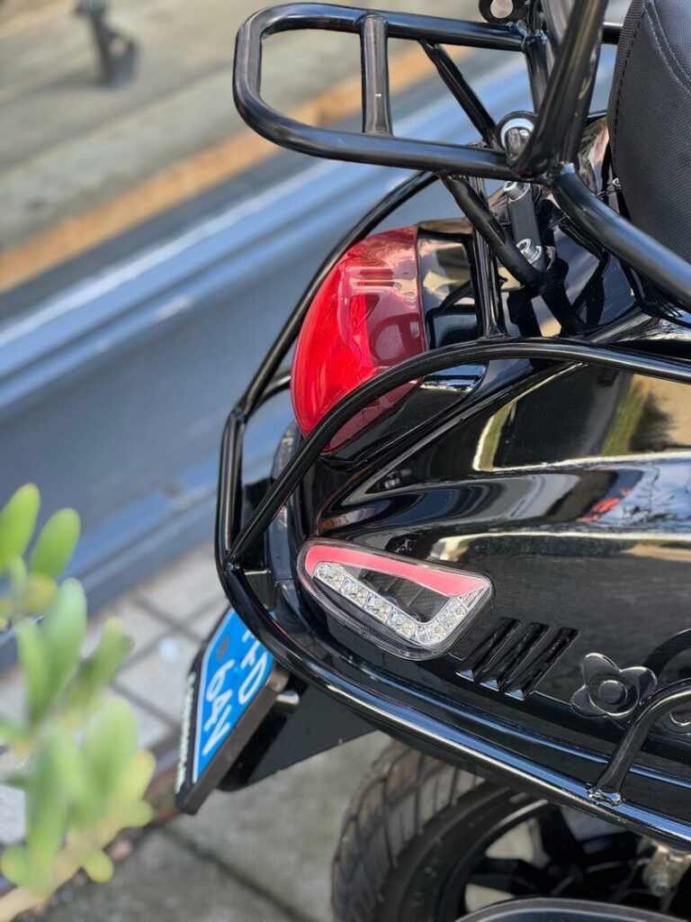 Close-up van de achterkant van een zwarte scooter met bagagerek, achterlicht en blauw kenteken.