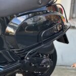 Close-up van de achterzijde van een glanzend zwarte scooter met zadel en wiel op straat.