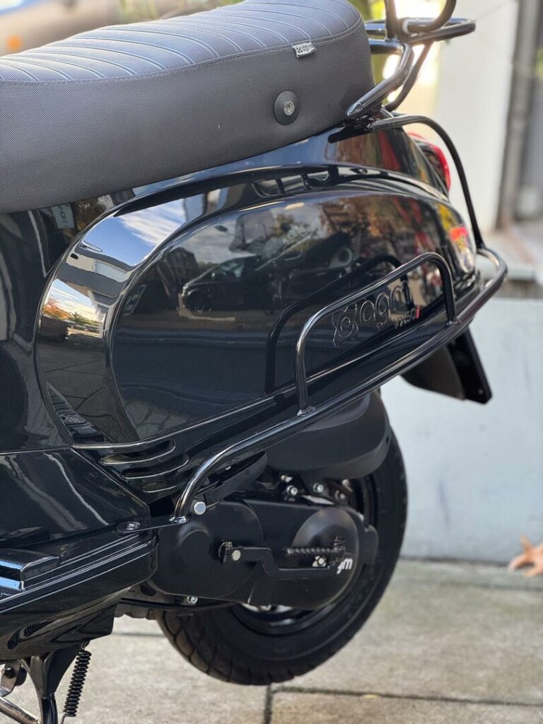 Close-up van de achterzijde van een glanzend zwarte scooter met zadel en wiel op straat.