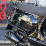 Close-up van de achterkant van een glanzend zwarte scooter met bagagerek en uitlaat.