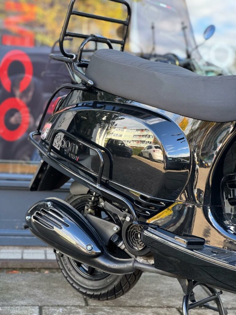 Close-up van de achterkant van een glanzend zwarte scooter met bagagerek en uitlaat.