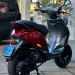 Rode en zwarte scooter geparkeerd op stoep, gezien van achteren met spiegels en kenteken.