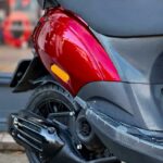 Close-up van de achterzijde van een rode scooter met zwart zadel, achterwiel en uitlaat.