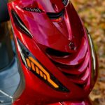 Close-up van de rode voorkant van een scooter met oranje LED-knipperlicht en ventilatieroosters.