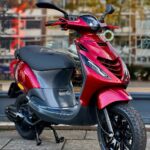 Glanzende rode scooter geparkeerd op de stoep voor een winkelraam.