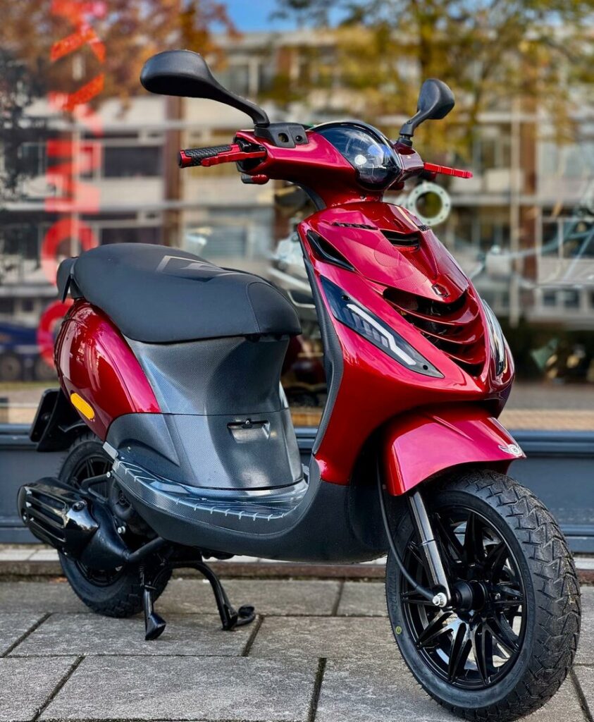 Glanzende rode scooter geparkeerd op de stoep voor een winkelraam.