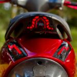 Close-up van de achterzijde van een rode scooter met rode LED-achterlichten en carbonlook panelen.