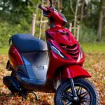 Rode scooter geparkeerd op herfstbladeren in een park, close-up van de voorkant.