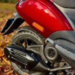 Close-up van de achterzijde van een rode scooter met wiel en uitlaat op herfstbladeren.