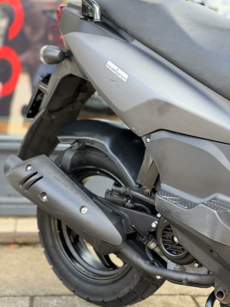 Close-up van de achterzijde van een grijze scooter met uitlaat, achterwiel en knipperlicht.