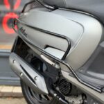 Close-up van de achterzijde van een grijze scooter met uitlaat, valbeugels en zwart zadel.