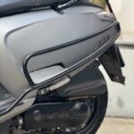 Close-up van de zijkant van een grijze scooter met beschermbeugel, zadel en achterwiel.