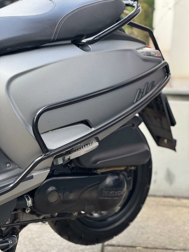 Close-up van de zijkant van een grijze scooter met beschermbeugel, zadel en achterwiel.